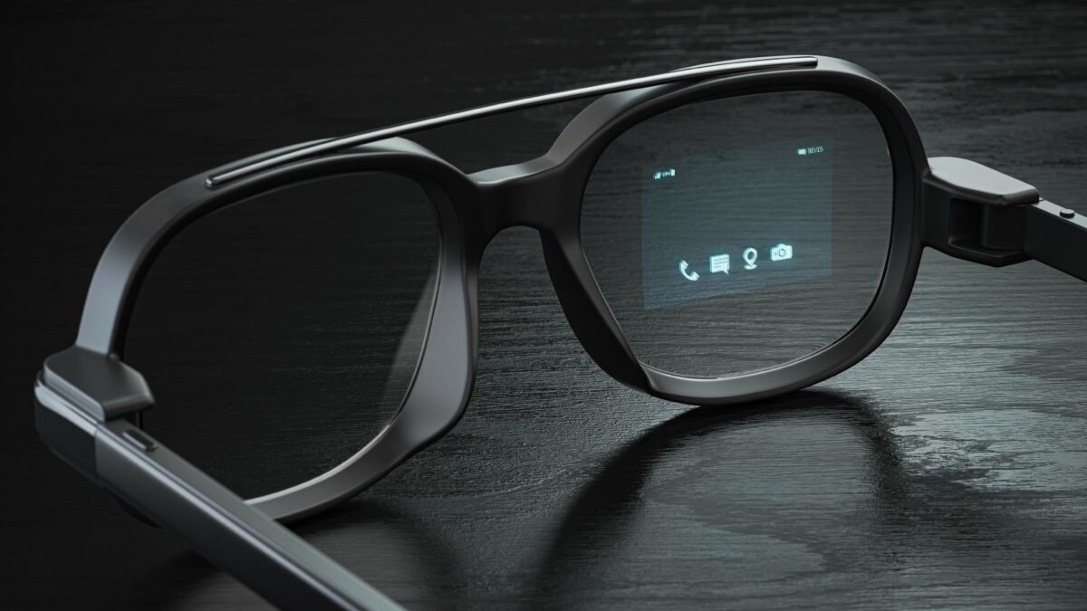 Les lunettes intelligentes Xreal Air 2 Pro AR à côté du hub Xreal Beam, elles sont toutes deux sur une table en bois devant un mur de briques