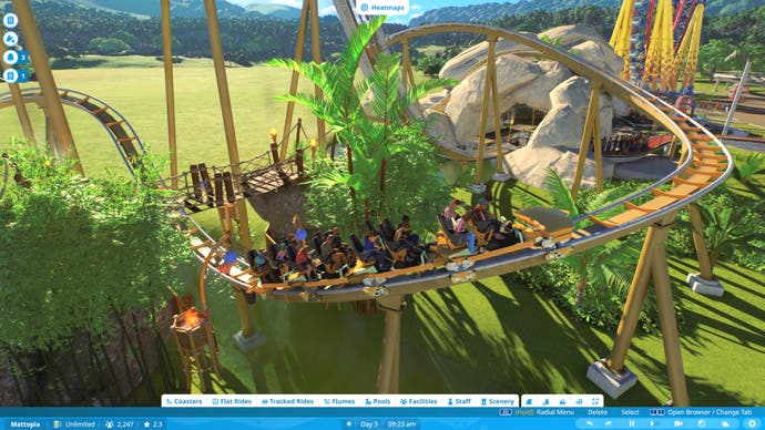 Capture d'écran de Planet Coaster 2 montrant un chariot de montagnes russes dévalant une piste alors qu'il surgit sous un pont en bois entouré d'arbres.